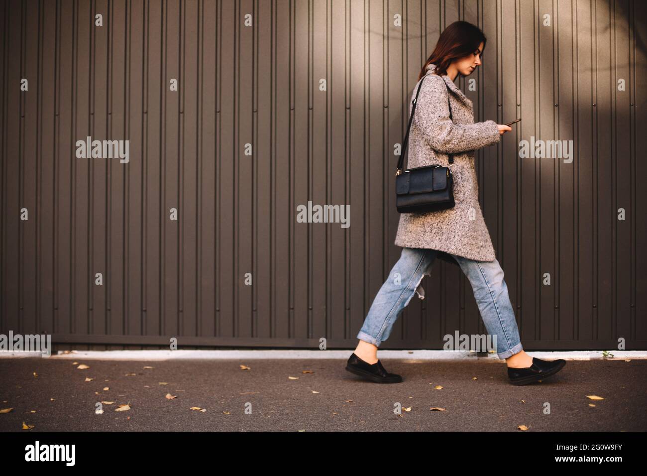 Side view of non-binary woman using smart phone walking against wall Stock Photo