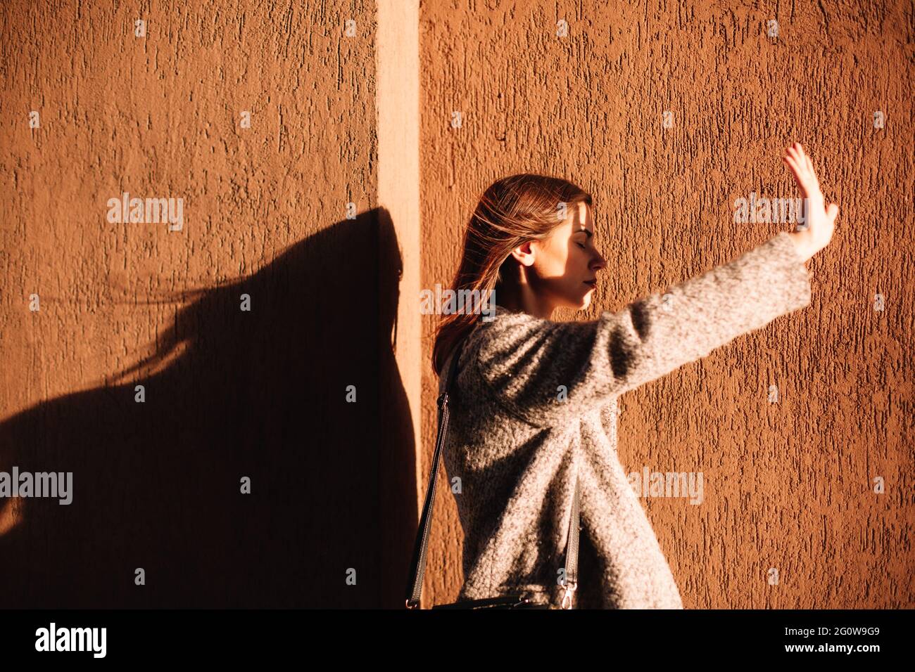 Young woman shielding eyes blocking sun against wall in city Stock Photo