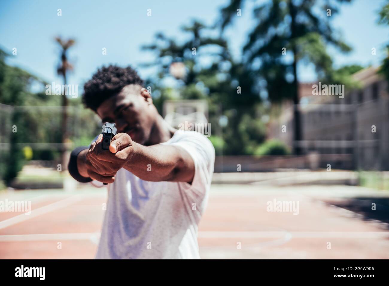Black African American boy on a basketball court aiming a gun at camera