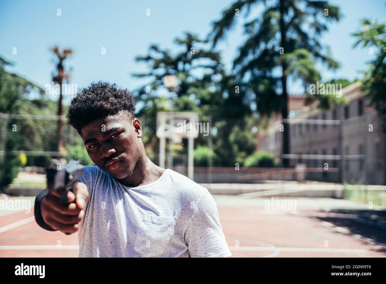 Black African American boy on a basketball court aiming a gun at camera