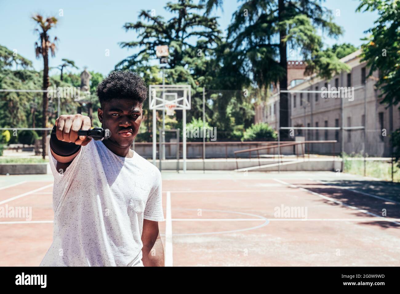 Black African American boy on a basketball court aiming a gun at camera