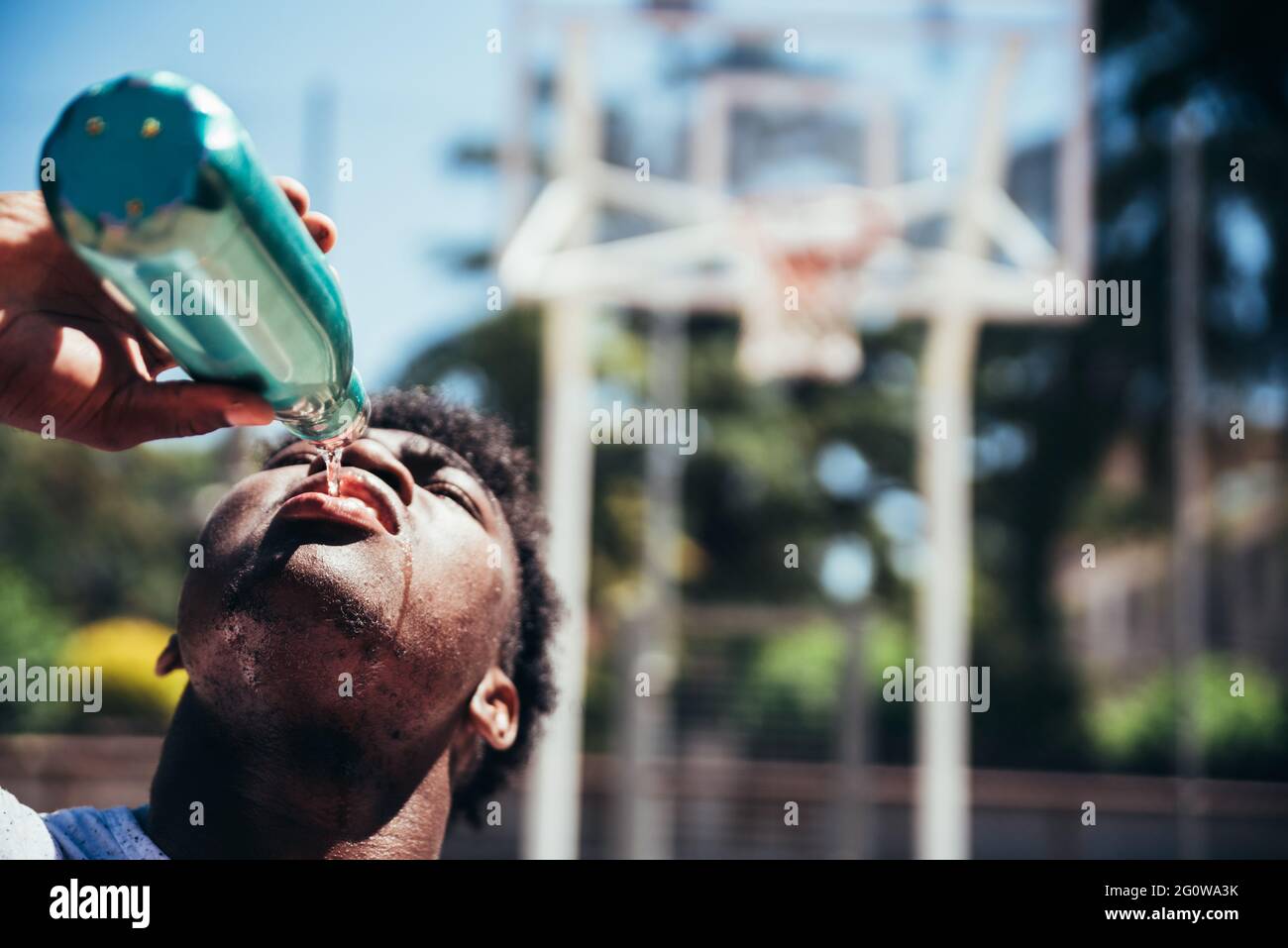 Portrait of an African-American black boy drinking water after training on an urban basketball court. Stock Photo
