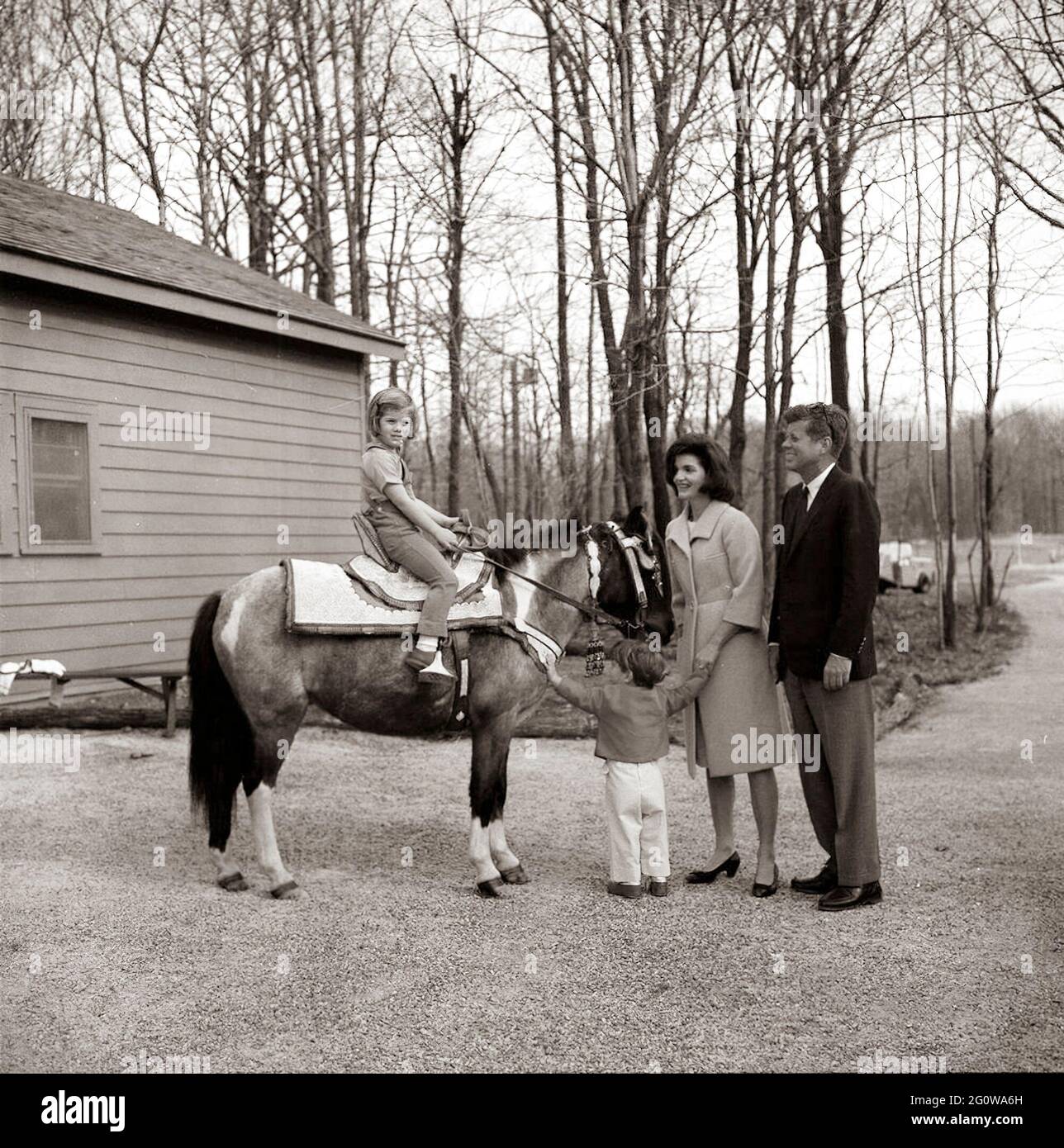 KN-C27672    31 March 1963  Weekend at Camp David. President John F. Kennedy and family watch Caroline Kennedy riding a horse named 'Macaroni' at Camp David.  'Macaroni' is wearing a blue and gold Moroccan saddle, a gift to President Kennedy from King Hassan II.  Photograph includes: (L-R) Caroline Kennedy, John F. Kennedy, Jr., First Lady Jacqueline Kennedy, and President Kennedy.  Camp David, Maryland.    Please credit 'Robert Knudsen. White House Photographs. John F. Kennedy Presidential Library and Museum, Boston' Stock Photo