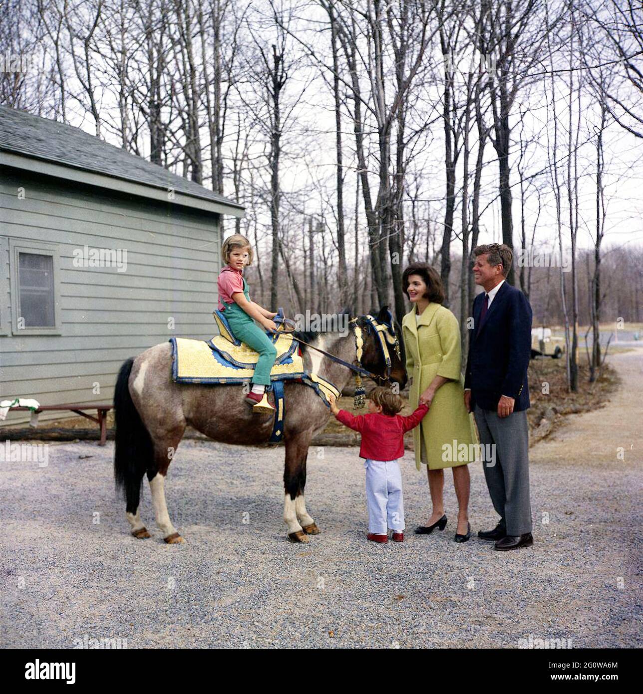 KN-C27672    31 March 1963  Weekend at Camp David. President John F. Kennedy and family watch Caroline Kennedy riding a horse named 'Macaroni' at Camp David.  'Macaroni' is wearing a blue and gold Moroccan saddle, a gift to President Kennedy from King Hassan II.  Photograph includes: (L-R) Caroline Kennedy, John F. Kennedy, Jr., First Lady Jacqueline Kennedy, and President Kennedy.  Camp David, Maryland.    Please credit 'Robert Knudsen. White House Photographs. John F. Kennedy Presidential Library and Museum, Boston' Stock Photo