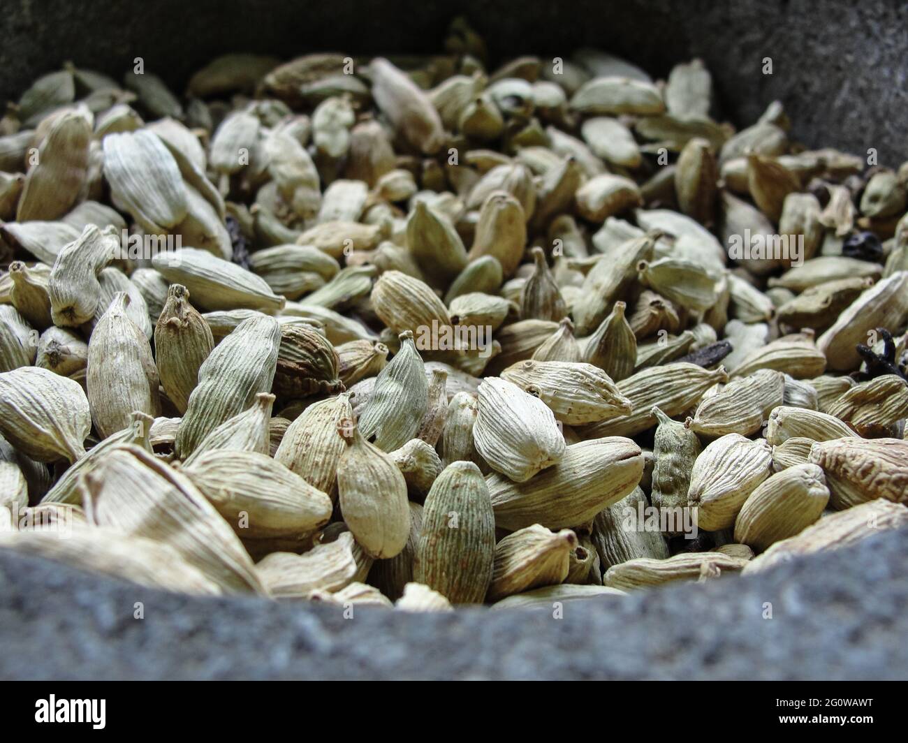 Green cardamom grains in a large stone mortar Stock Photo