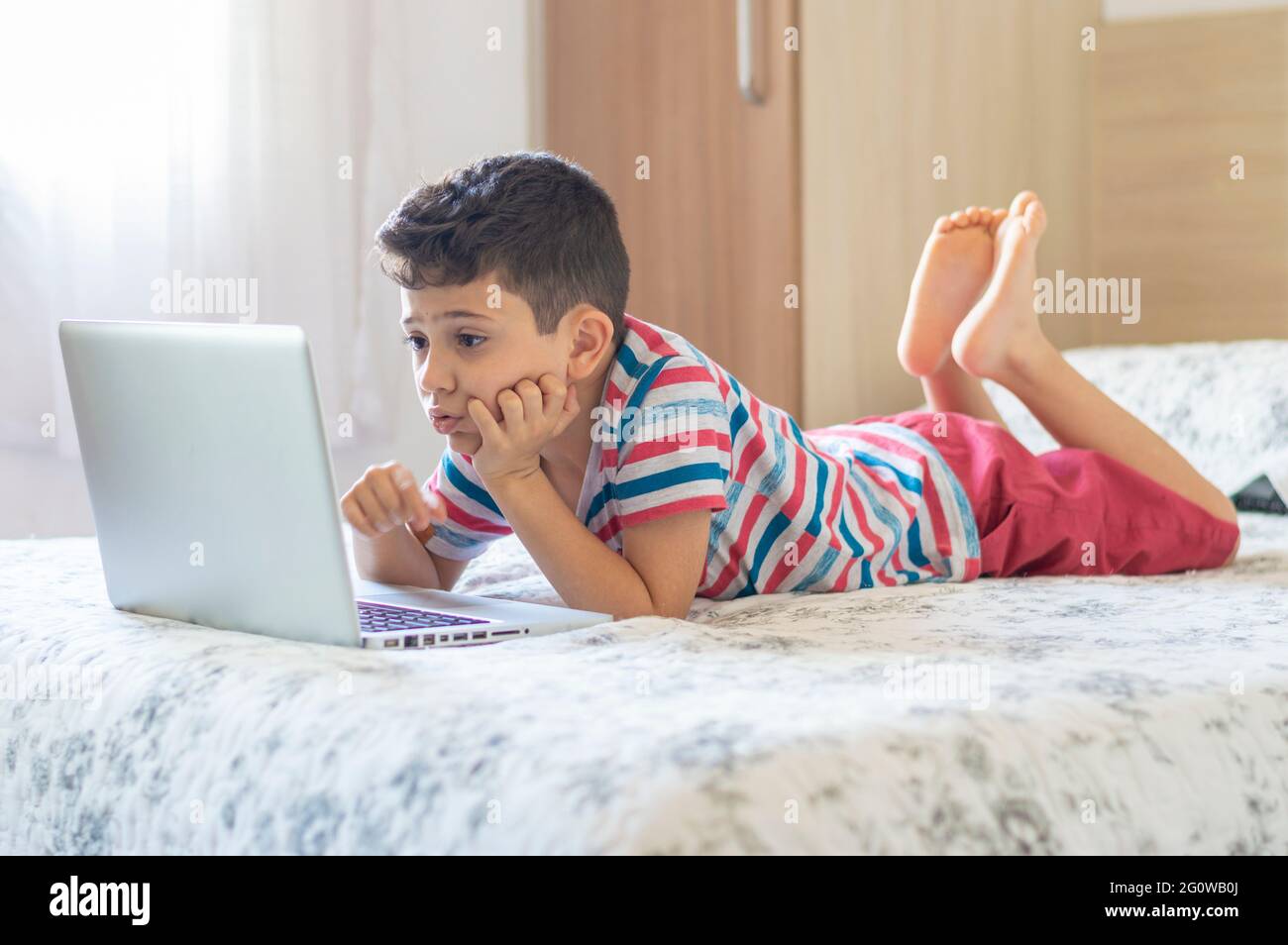 Young boy child lying on bed using a laptop. Online class lesson Stock Photo