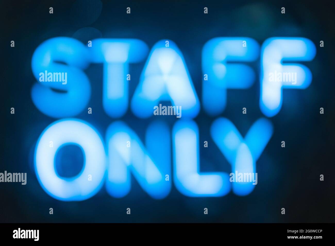 Blurred neon letters, signboard staff only on a black wall close-up. Stock Photo