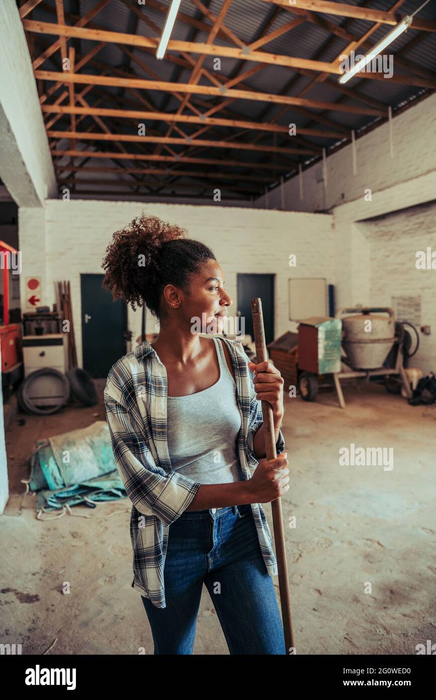 Mixed race female sweeping farm barn room after dusty day in storeroom Stock Photo