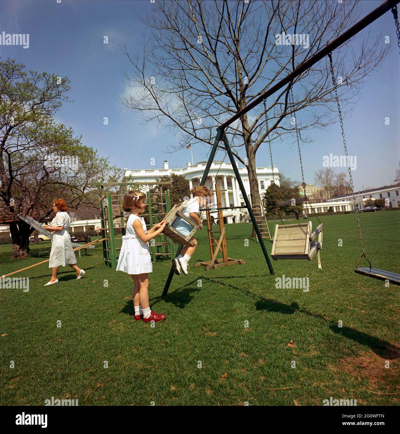 ST-C66-13-63                                                    1 April 1963   Caroline Kennedy pushes John F. Kennedy Jr. on the swing on the South Lawn. Also pictured: Nurse Maude Shaw.   Please credit 'Cecil Stoughton. White House Photographs. John F. Kennedy Presidential Library and Museum, Boston' Stock Photo