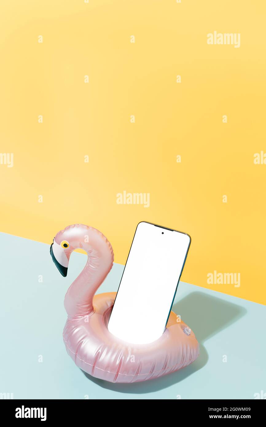 inflatable in the shape of a pink flamingo with a mobile inside on a blue and yellow background. Summer holiday and travel concept background. vertica Stock Photo