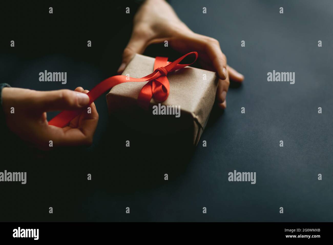 Packing gift box in organic paper on black background. Home made christmas decoration and gift concept. Stock Photo