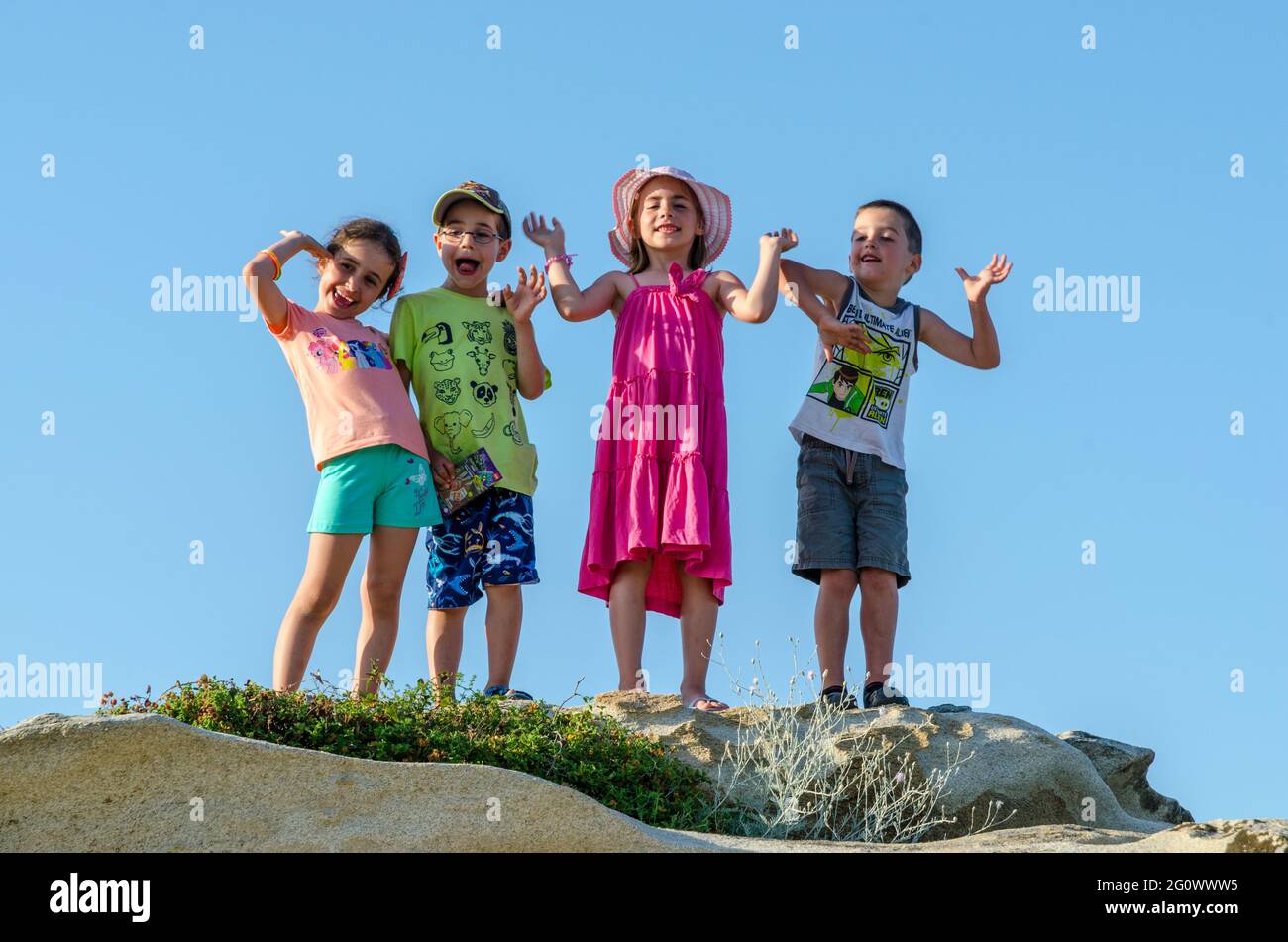 Four happy children, two girls and two boys, climbed on a rock, express ...