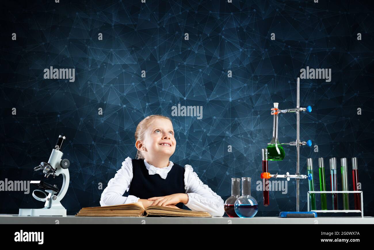Smiling little girl sitting at desk with open book Stock Photo - Alamy