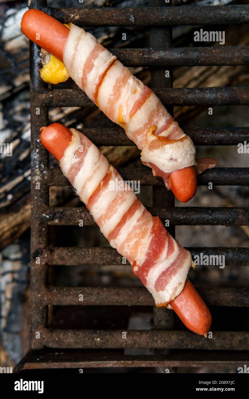 Bacon wrapped cheese hot dogs roasted over campfire wood Stock Photo