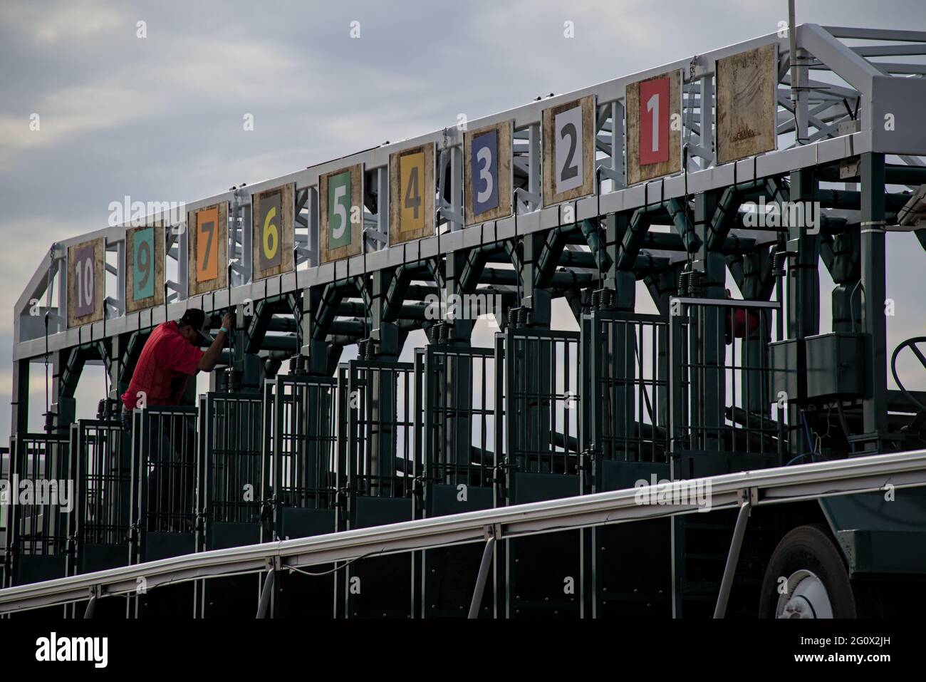Horse racing gate chute being prepped for the next race by worker changing numbers and closing doors while horses prepare to enter. Stock Photo