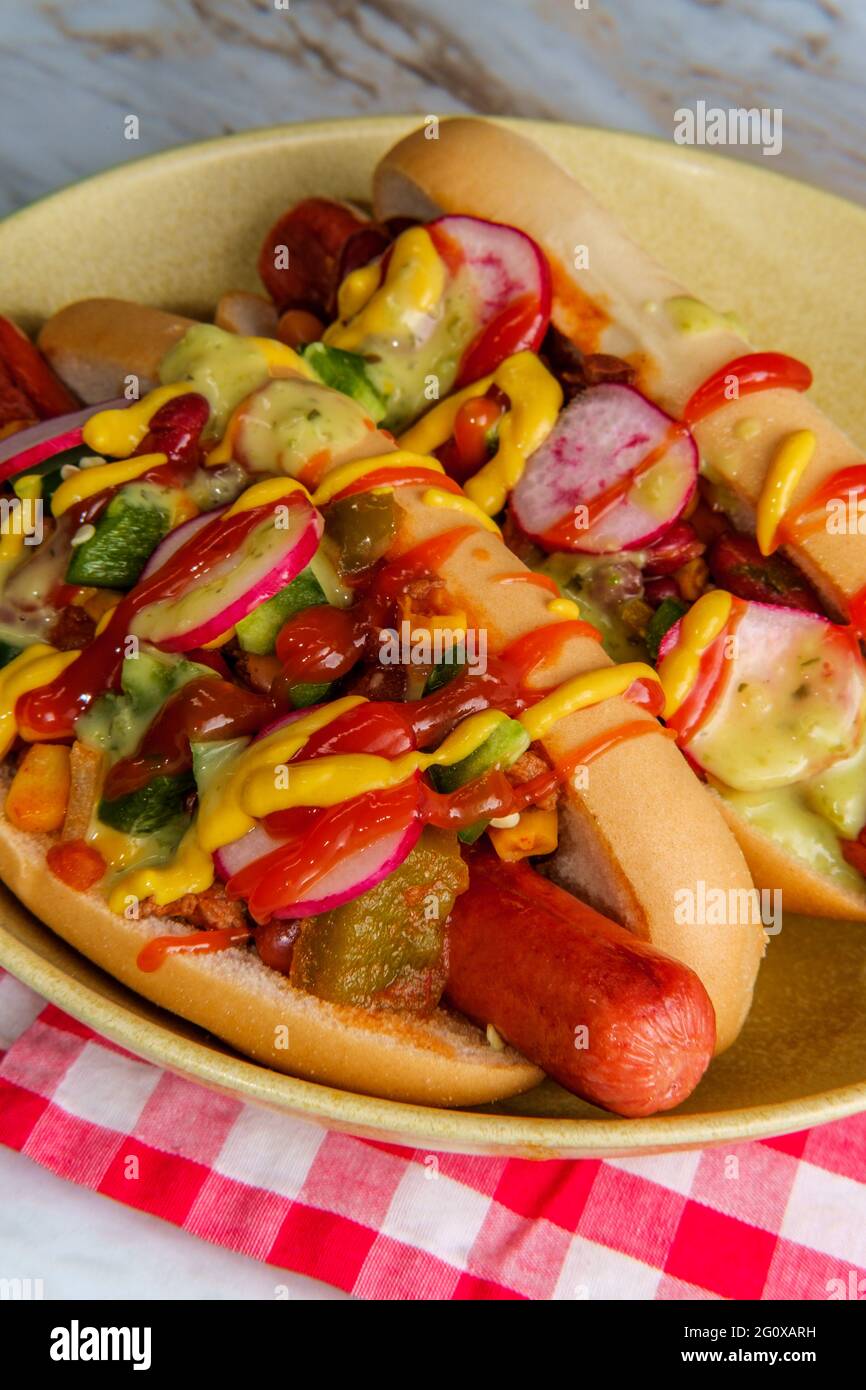Fancy chili dogs topped with radishes mustard ketchup and green sauce