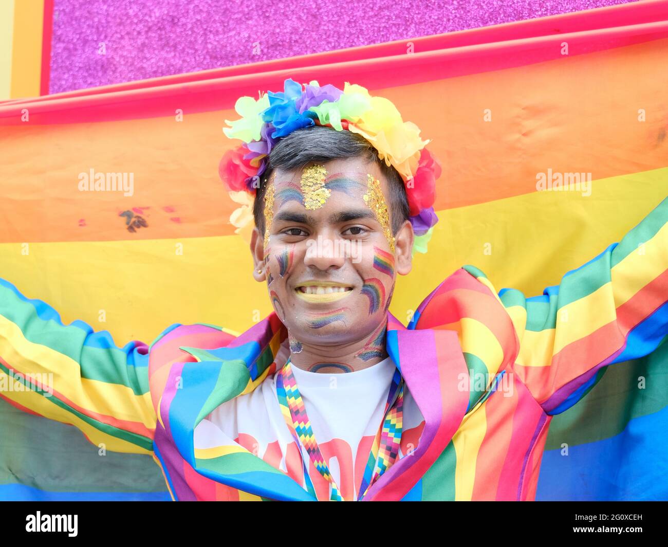 A Jubilee Pride in London participant holding a LGBT rainbow flag and dressed in a rainbow suit smiles for the camera. Stock Photo