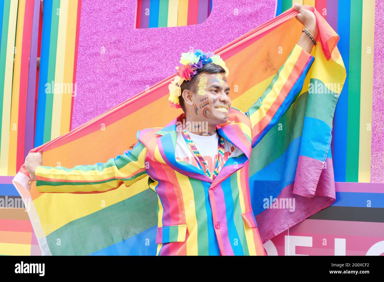 A Jubilee Pride in London participant holding a LGBT rainbow flag and dressed in a rainbow suit smiles for the camera. Stock Photo