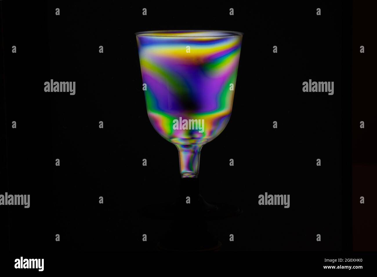 Transparent hovering plastic cup, polarized rainbow colored isolated on black background. Synthwave modern futuristic look. Stock Photo