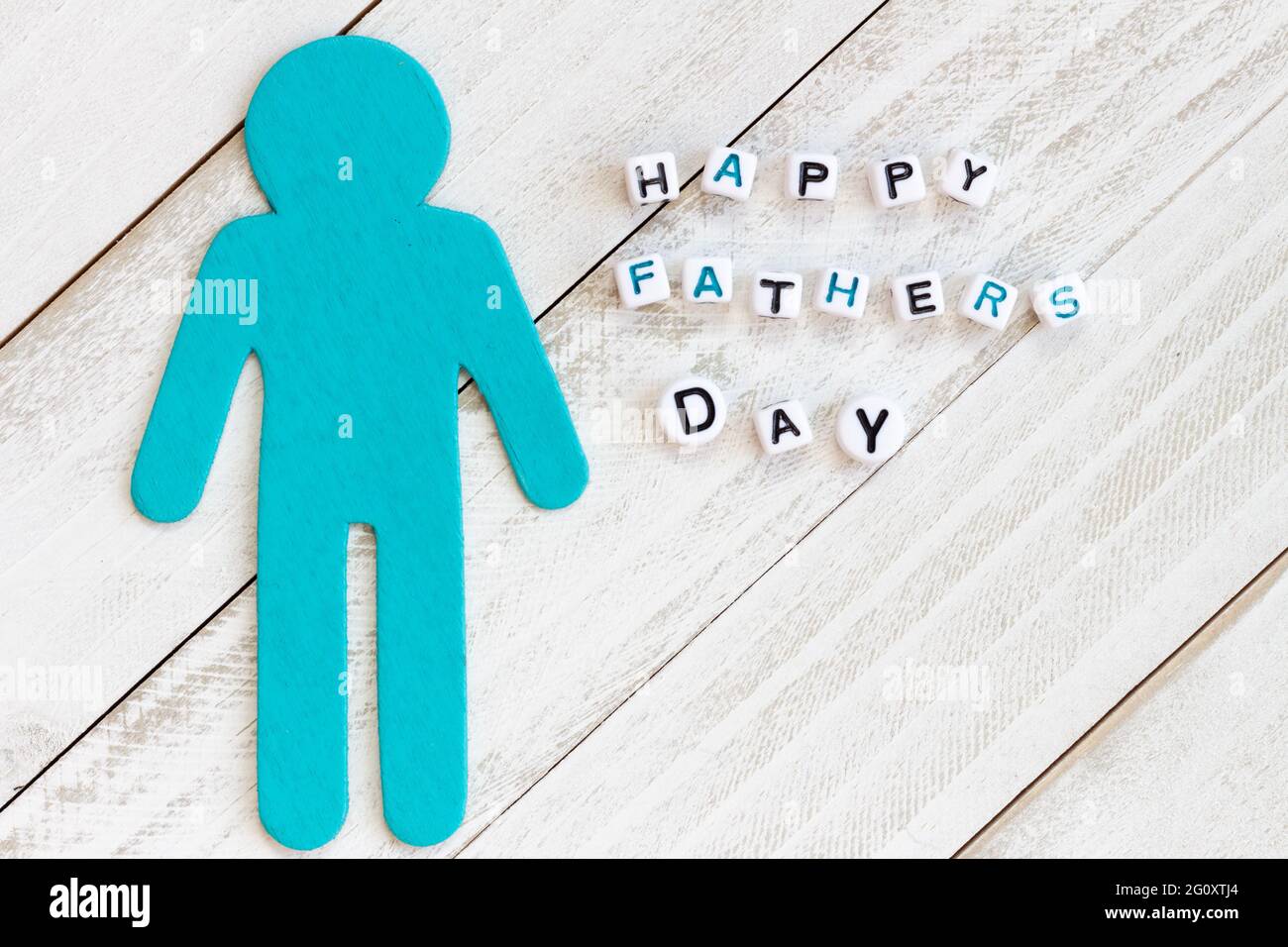 Happy Fathers Day written in bead blocks with teal man symbol cut out on white wood background Stock Photo