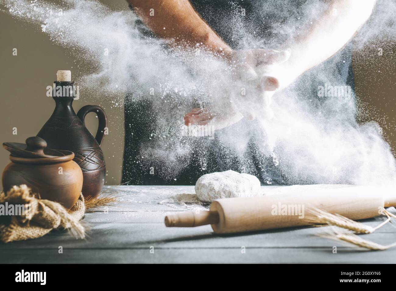 Male hands with flour clap over dough next to clay pot and oil bottle ...