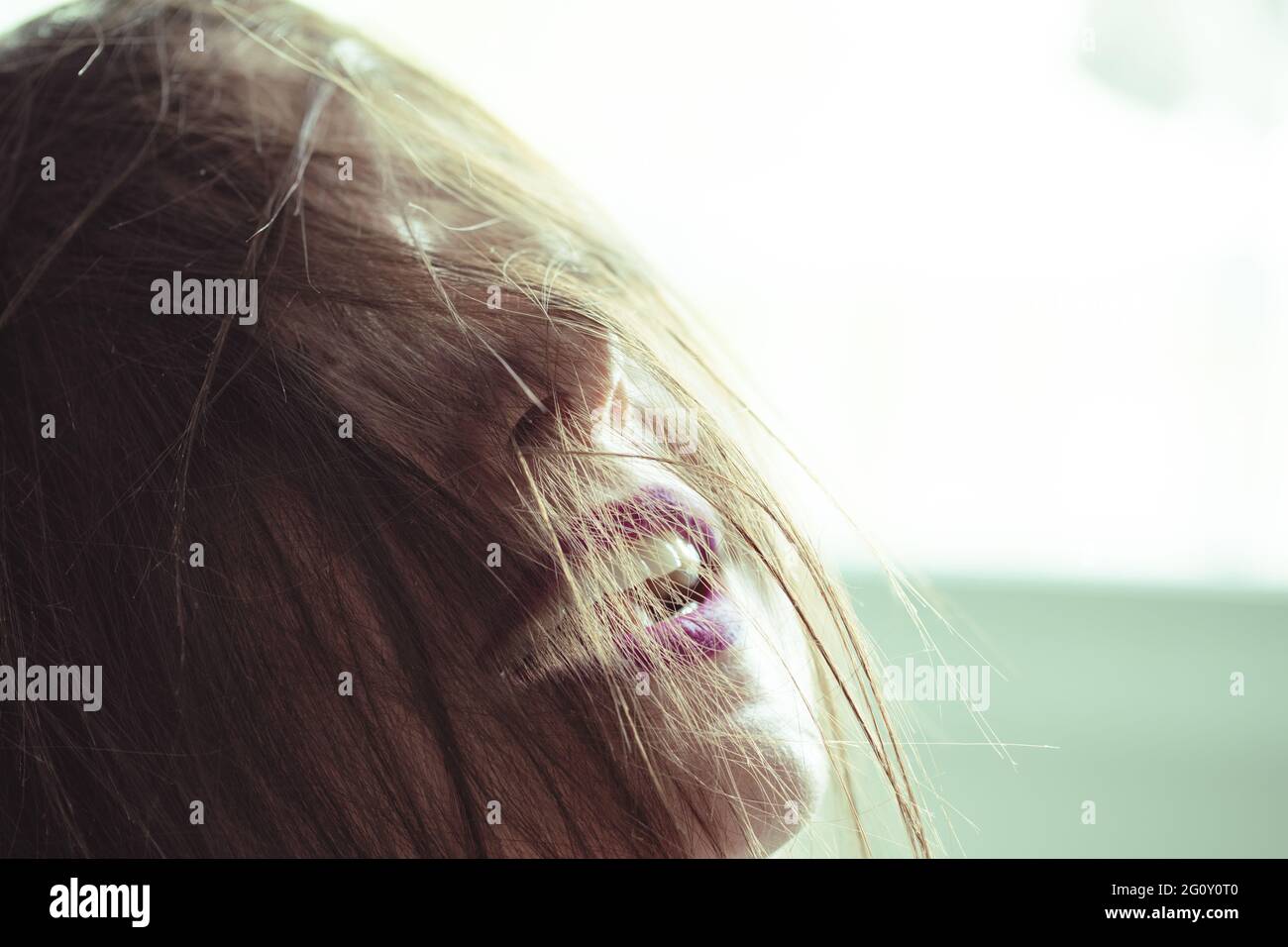 messy hair in the face of a woman with back light and purple lipstick on smiling lips Stock Photo