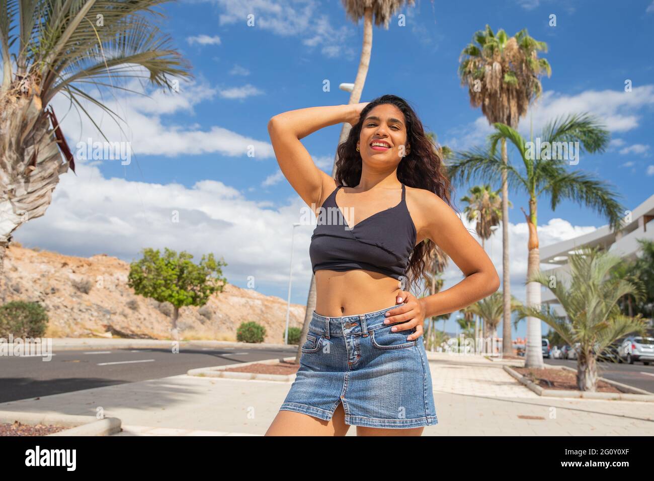 Latin girl enjoys her vacation in a tropical resort with palm trees, she is in tenerife, the sky is clear, she is attractive, happy and smiling Stock Photo