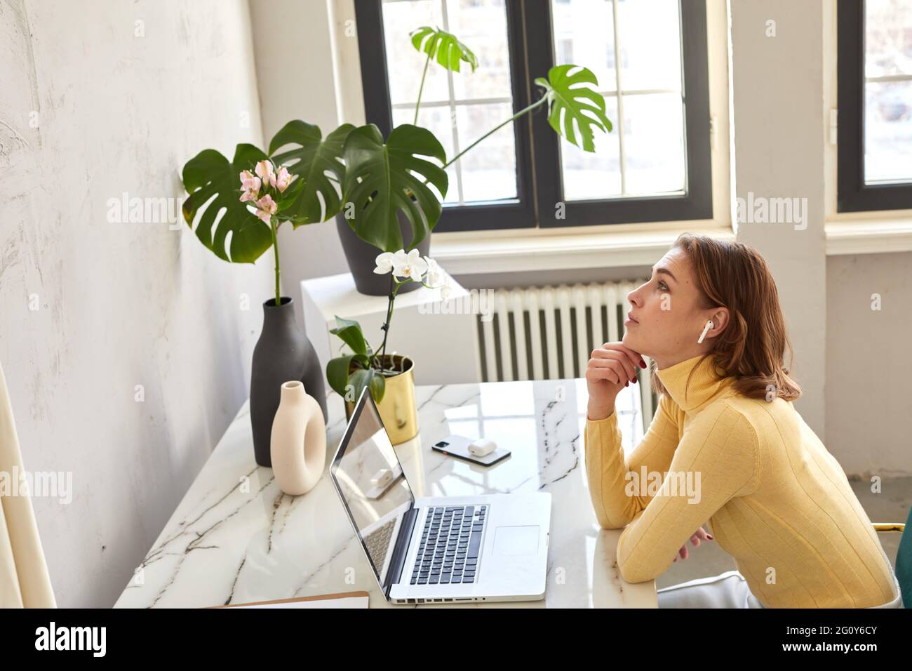 Side view of female in wireless earphones sitting at table with netbook and enjoying music and looking up Stock Photo