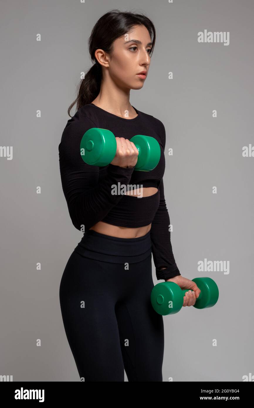 Athletic girl performing dumbbell bicep curl on grey background Stock ...