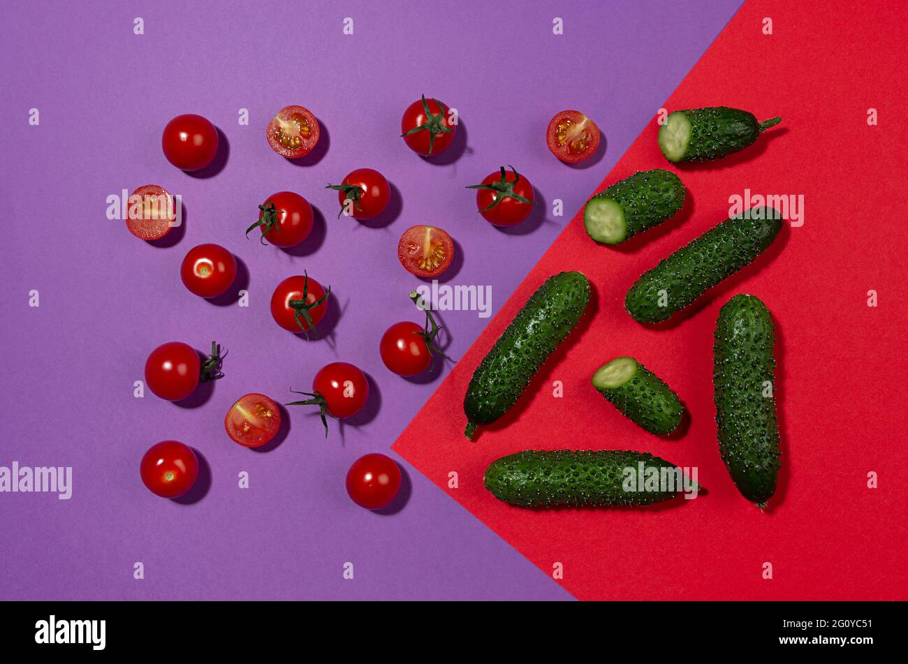 Juicy red tomato, green young cucumber with shadow on contrast red and purple background. Modern food pattern, top view. Stock Photo