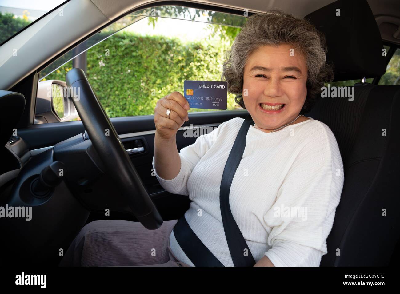 Happy senior Asian woman sitting inside car and showing credit card pay for oil, pay a tire, maintenance on the garage, Make payment for refueling car Stock Photo