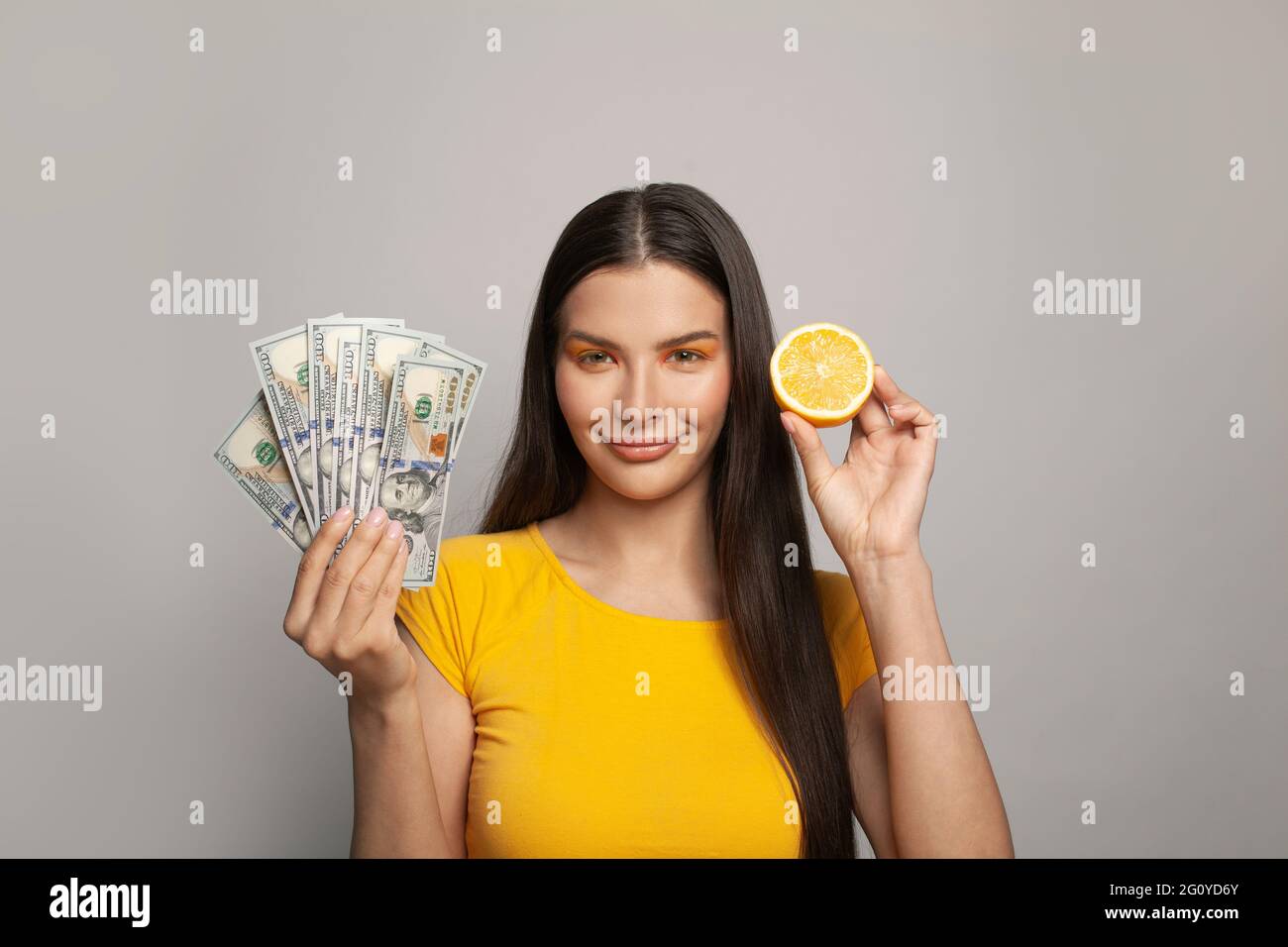 Attractive gorgeous young amazed woman wearing yellow t-shirt with dollar banknotes. Young female model holding money banknotes and celebrating isolat Stock Photo