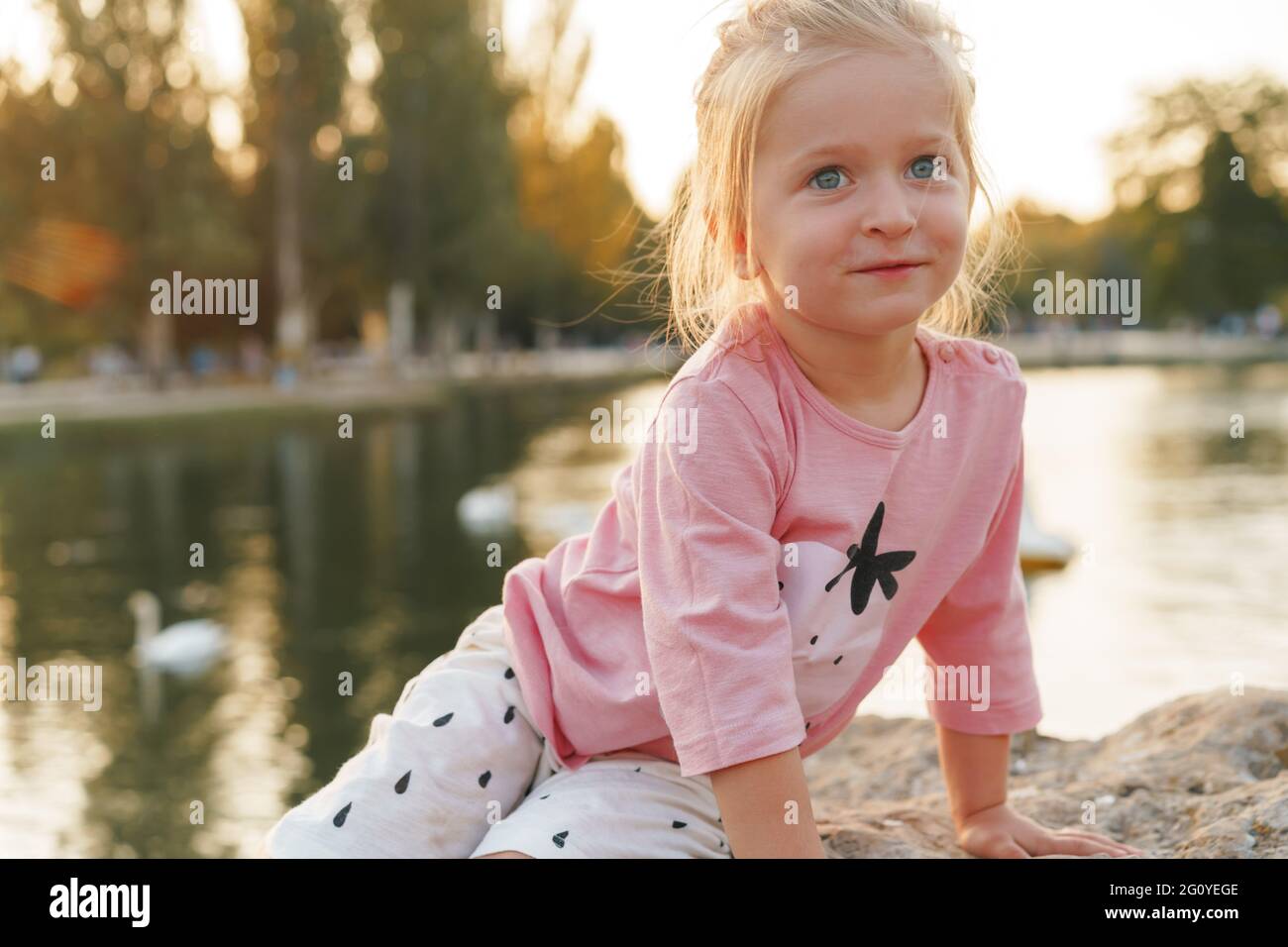 Little girl sitting on a huge stone in park near the lake Stock Photo ...