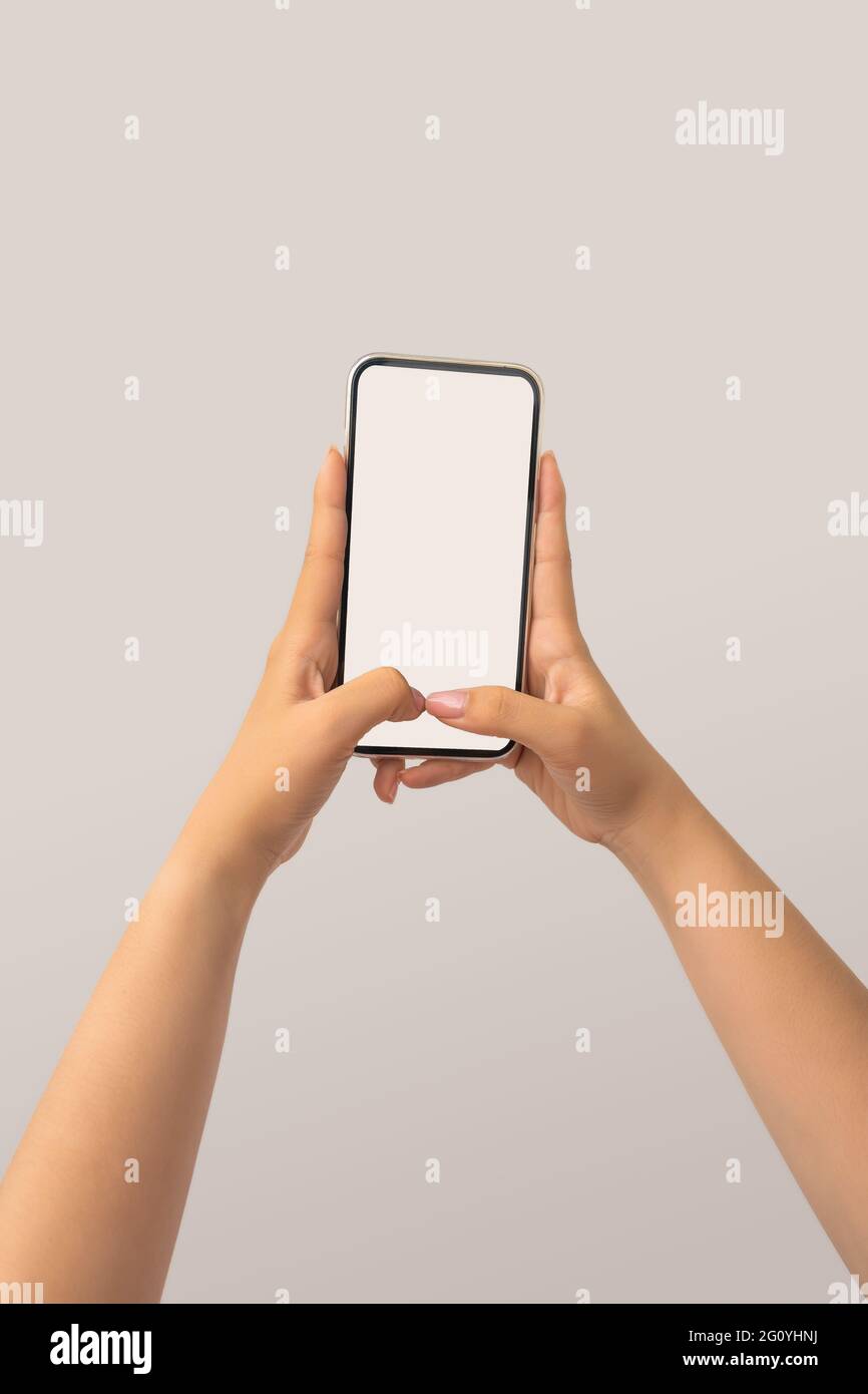 Closeup shot of a woman typing on mobile phone isolated on white background.. Girl's hand holding a modern smartphone and pointing with figer. Blank s Stock Photo