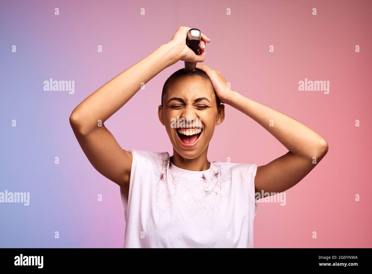Woman trimming her head to bald on multicolored background. Female shaving off her hair with hair clippers. Stock Photo