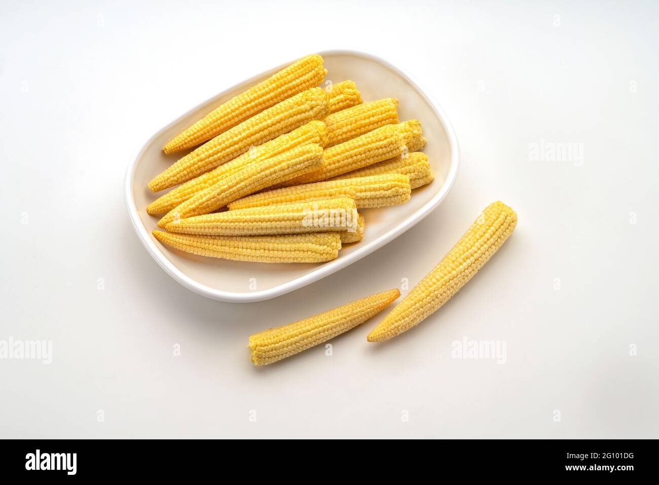 Closeup top view showing Baby Sweet Corn,Maize,Zea Mays in white ceramic dish displayed against white background, Stock Photo