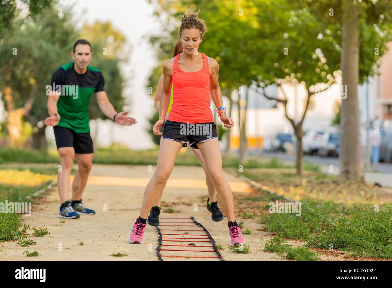 Focused woman doing fitness circuit in the park and working out with her personal trainer. Stock Photo