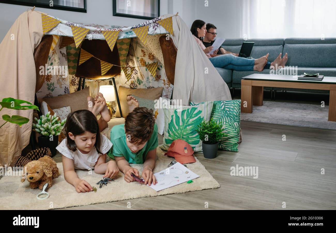 Children playing camping at home while their parents work with laptop Stock Photo