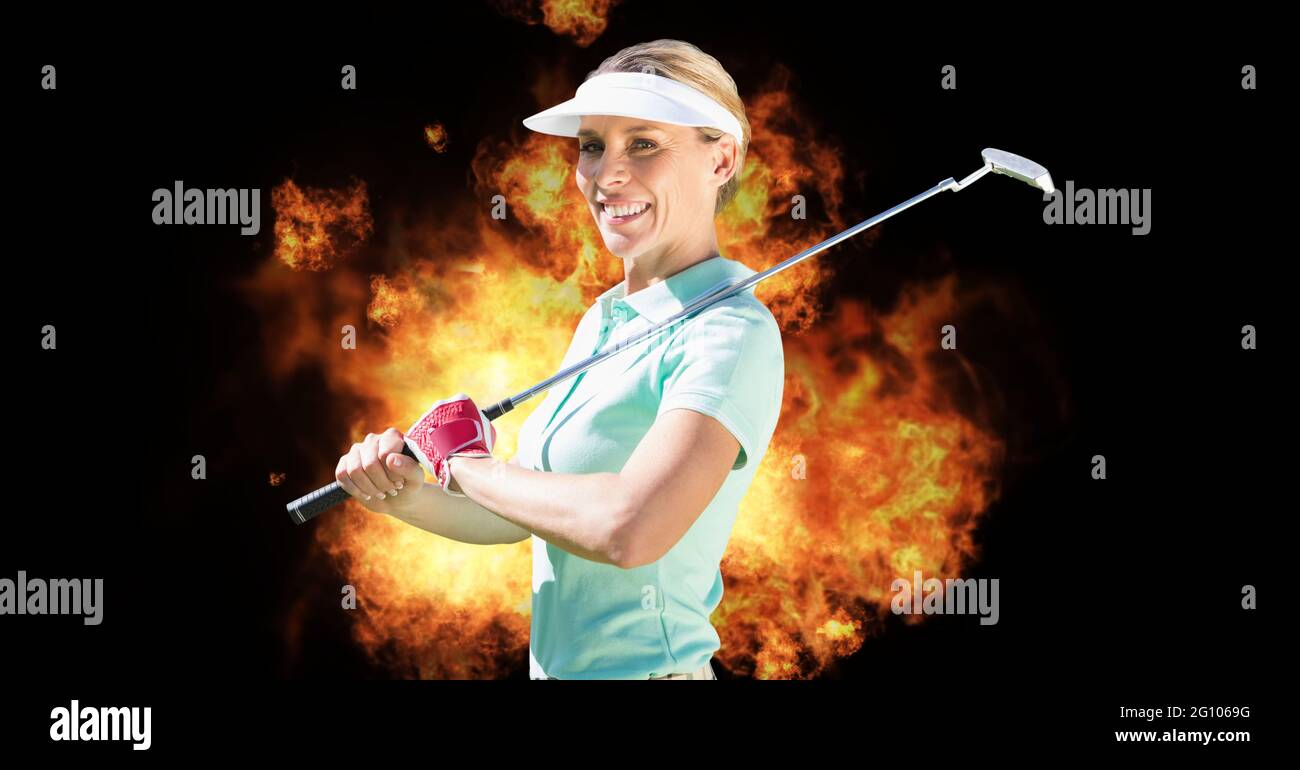 Composition of smiling caucasian female golf player with golf club over flames on black background Stock Photo