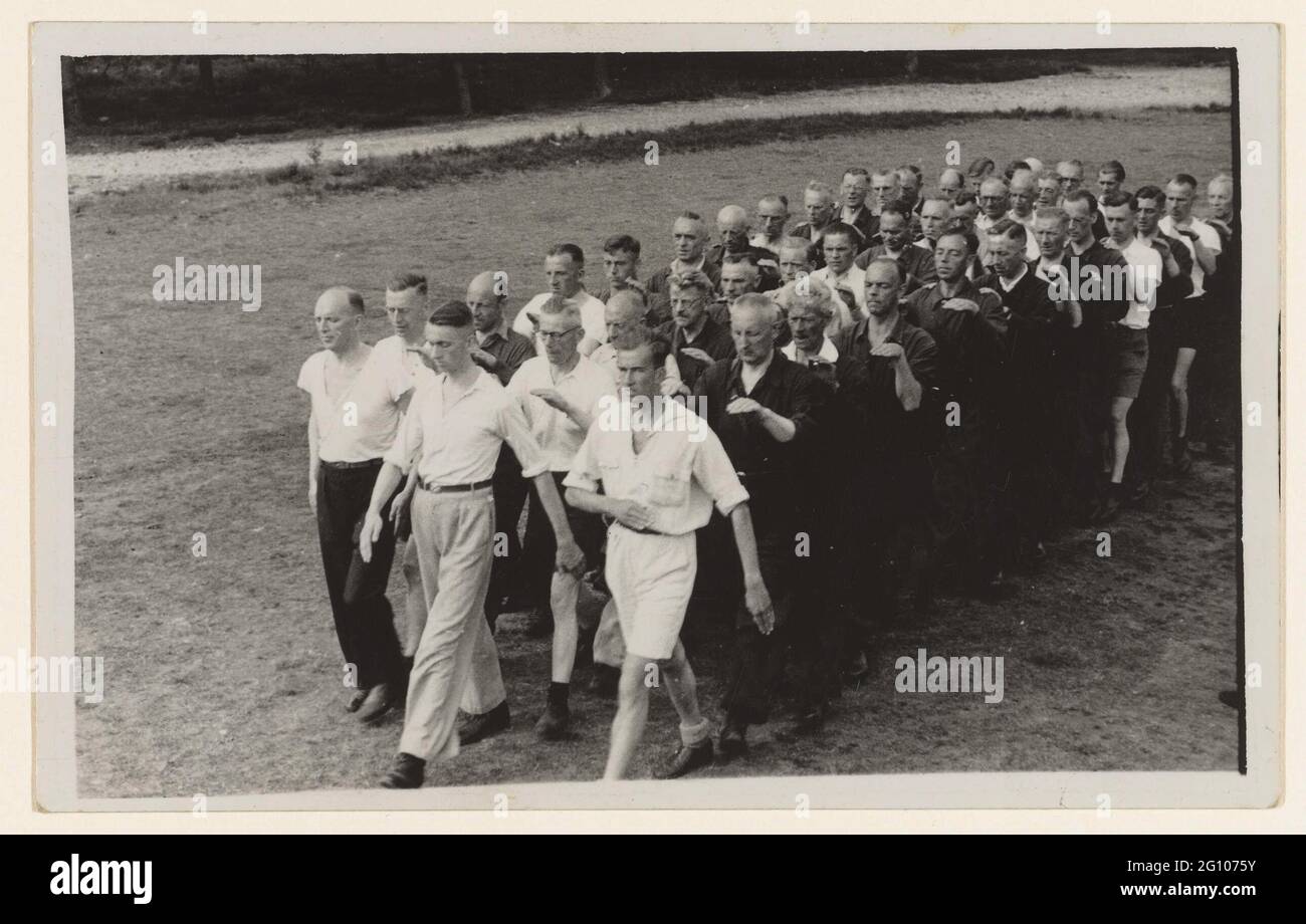 Training country guard; NSB. Three rows of men walk over a lawn. Hands on the man's shoulders for him. On the right men in overalls, some others in shorts or long pants. The men are trained at De Scheleberg in Lunteren for the country guard. Founded in November 1943 as a protection organization for the NSB after a number of attacks on leading Nsbers. Soon the land guard came under control of the Germans and was also used as a help police. The Scheleberg was built as a resort for members of the General Association for trade and office workers. Stock Photo