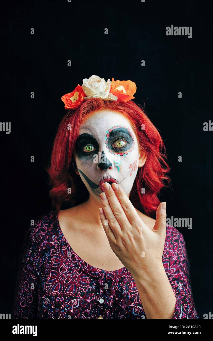 A young woman in day of the dead mask skull face art. Red-head model wear sugar skull makeup. Stock Photo
