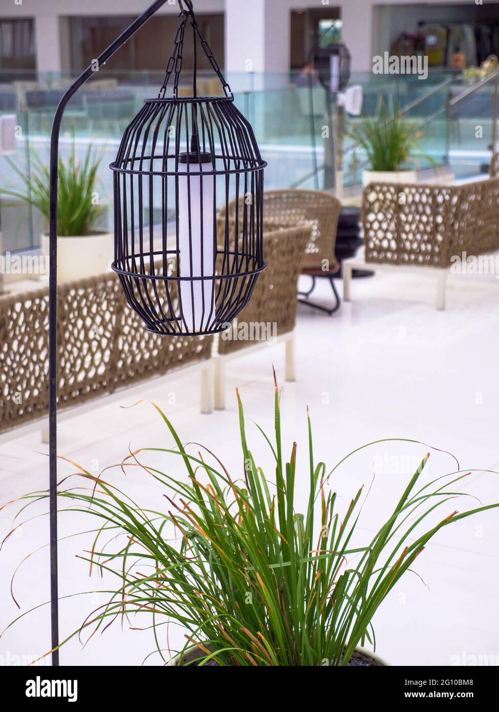 High black metal grid lantern hanging near the empty rattan wicket brown chairs without people standing on an empty hotel terrace after the rain. Stock Photo