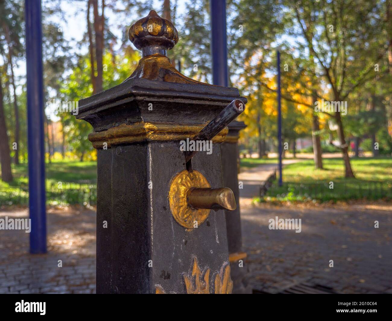 Old-fashioned public metal hand water pumps with golden decoration to draw up clean well water for people to drink and collect it in bottles. Stock Photo