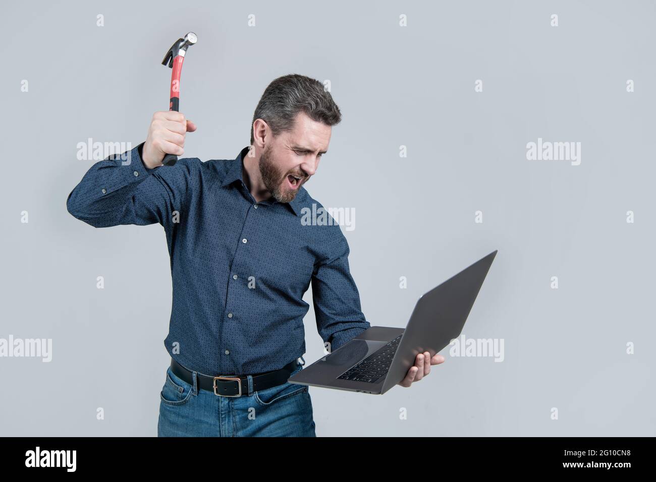 Yelling engineer break laptop computer with hammer grey background, frustration Stock Photo