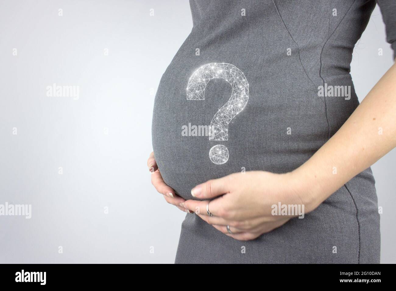 Young woman holding pregnant belly in hands with hologram question mark. Pregnancy, maternity concept. Close-up, copy space. Stock Photo