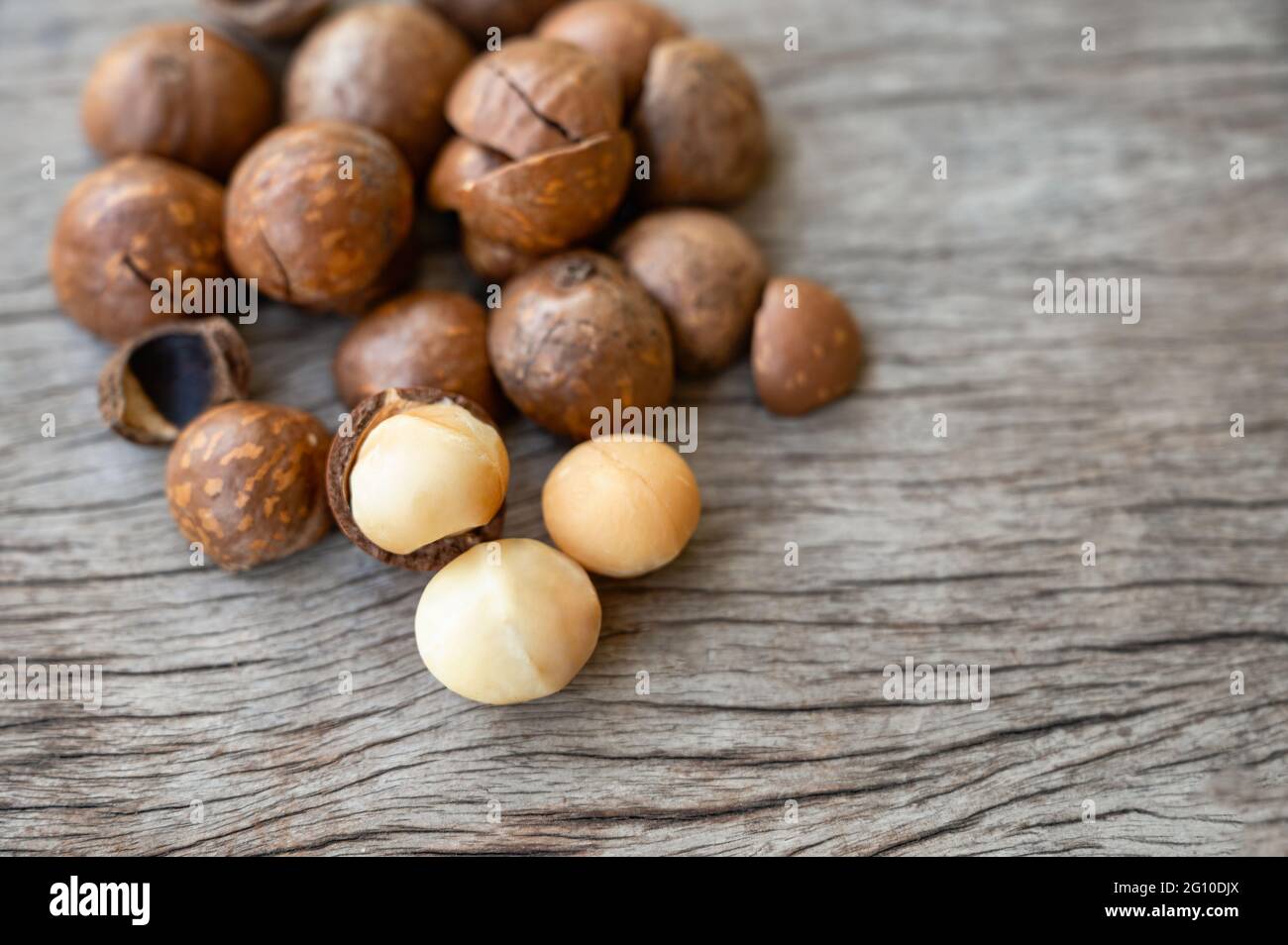 Organic Macadamia nuts with shell on wooden table Stock Photo