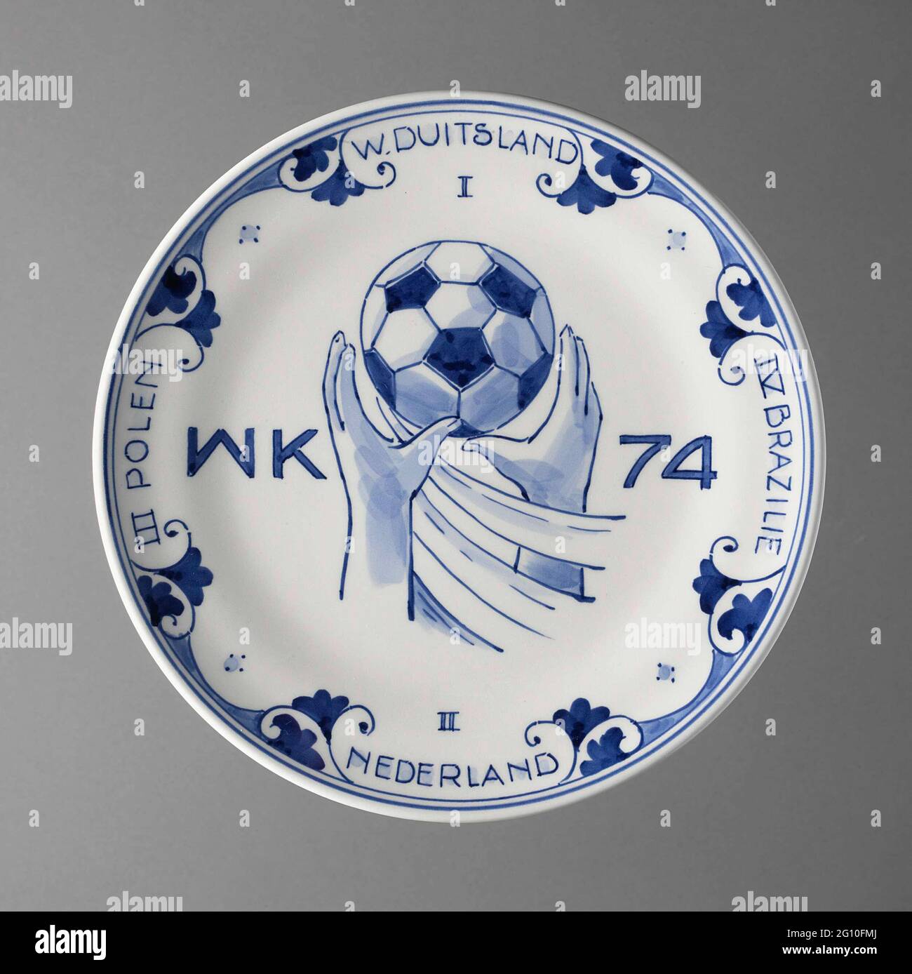 Football world championships, 1974. Plate, blue painted with image of two hands to clamp a football: a throw. With inscription: the countries that have been sinned in the first four places. The Netherlands was second after 2-1 defeat against West Germany. Back two blue edges and v.z.v. Two holes and iron wire to hang plate. Signature. Stock Photo