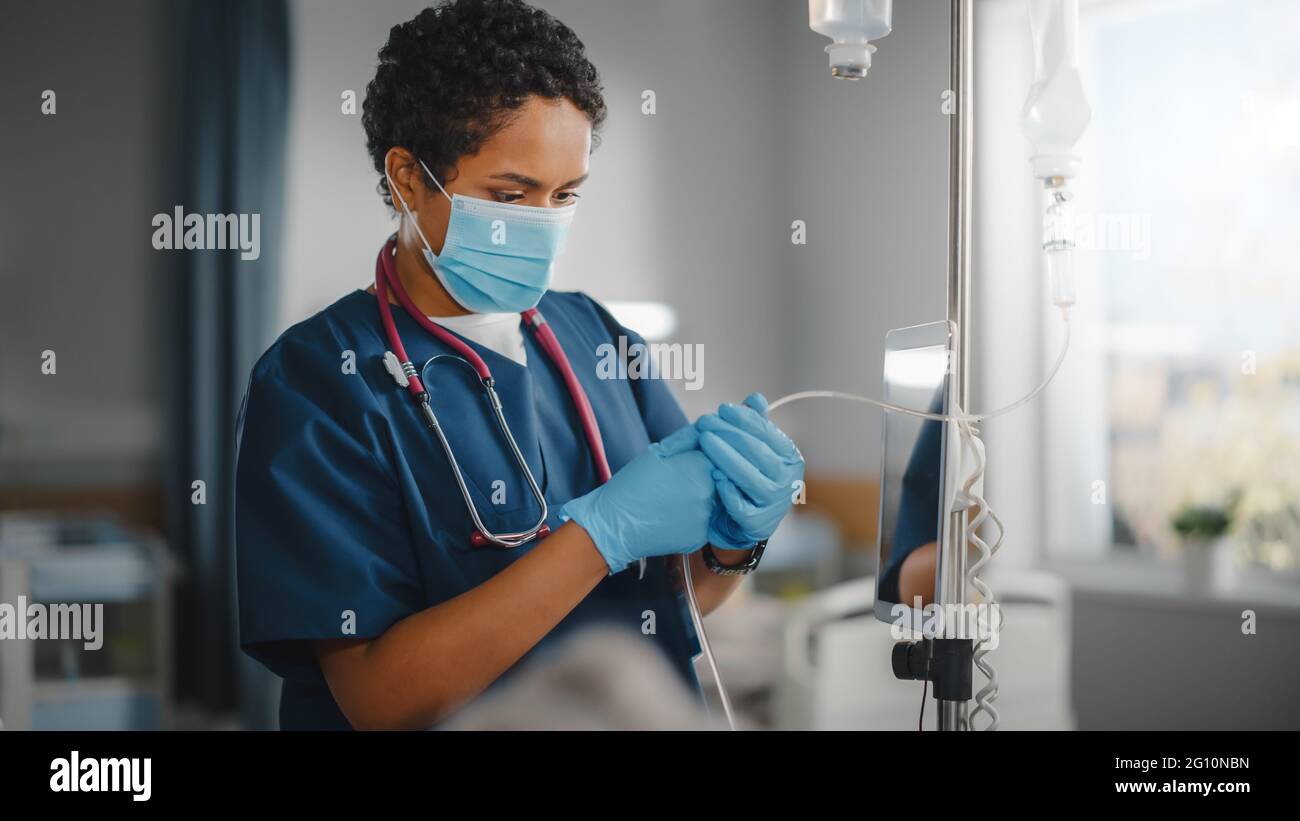 Hospital Ward: Professional Black Head Nurse Wearing Face Mask Does Checkup of Patient's Vitals, Checking Heart Rate Computer, Intravenous or Iv Stock Photo