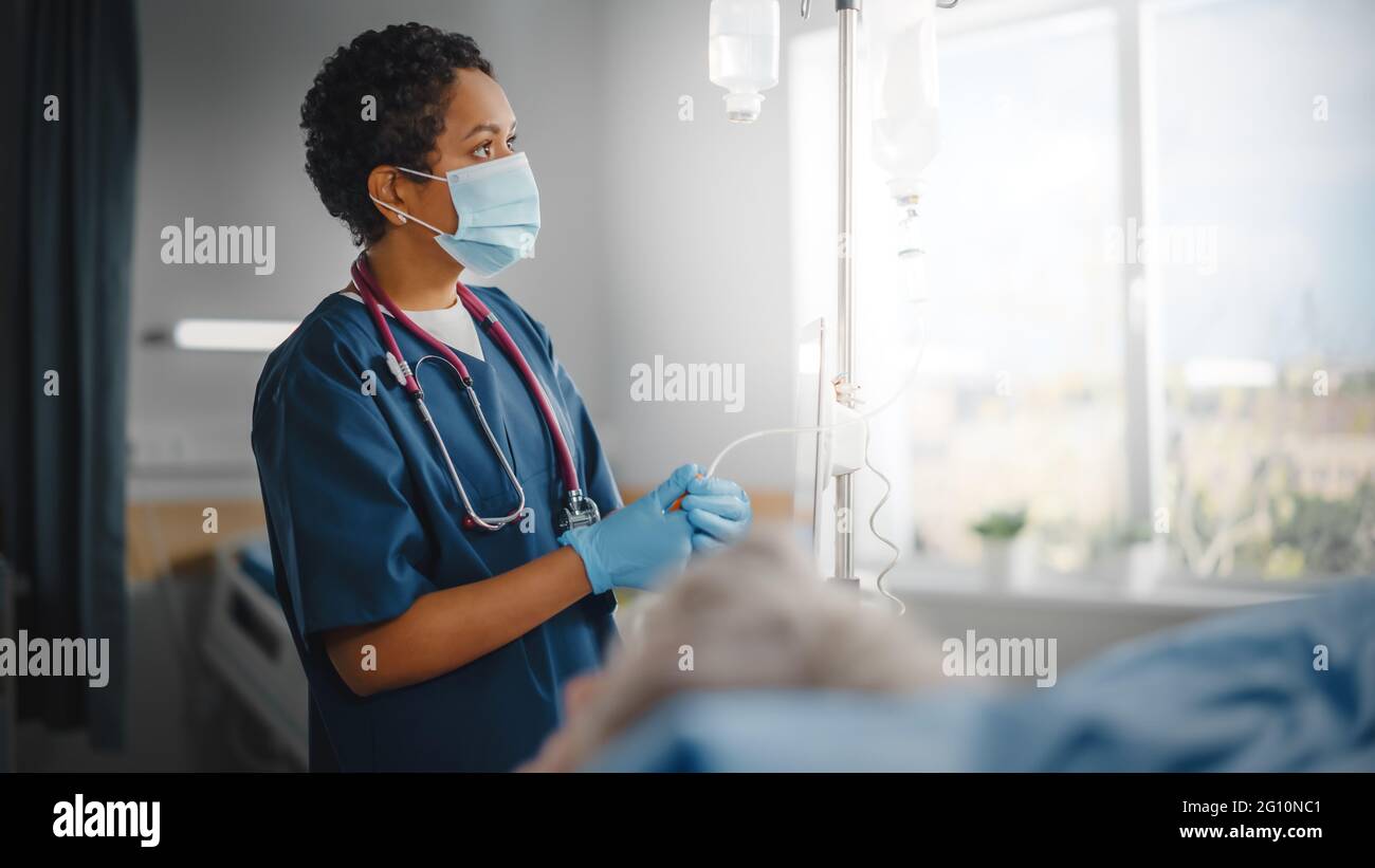 Hospital Ward: Professional Black Head Nurse Wearing Face Mask Does Checkup of Patient's Vitals, Checking Heart Rate Computer, Intravenous or Iv Stock Photo