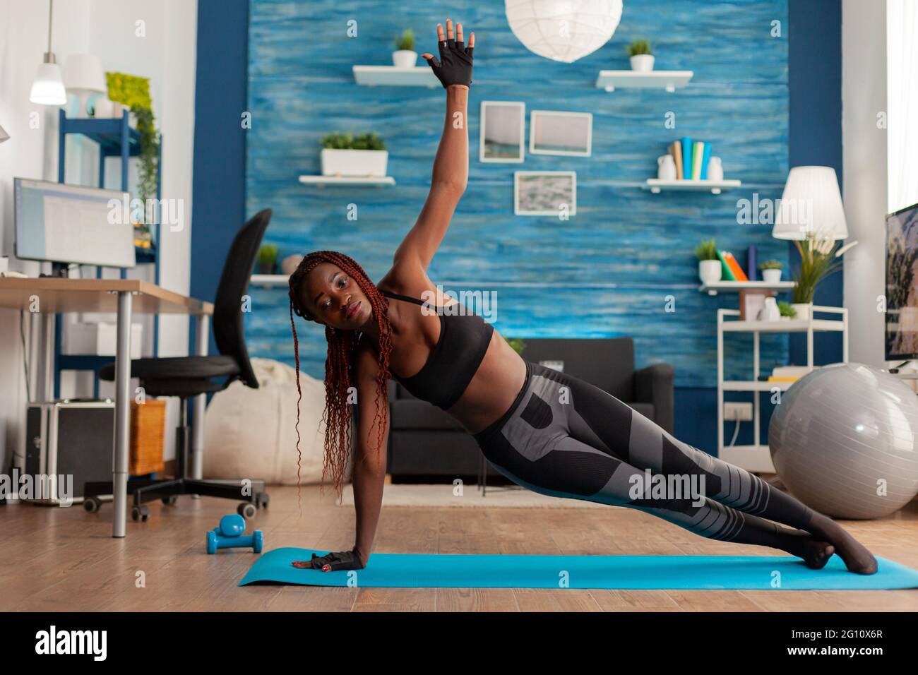Fit athletic black woman standing in side plank on yoga mat in home living room, doing strenght exercises, training for healthy lifestyle. Full lenght of african american working out. Stock Photo